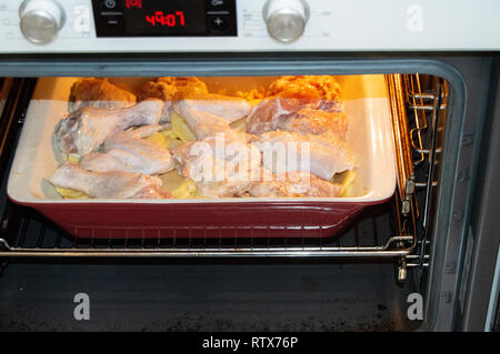 Leckere hausgemachte Braten mit Huhn und Kartoffeln, rohe Zutaten in einem keramischen Pfanne im heißen Ofen ein Abendessen mit der Familie Stockfoto