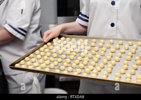 Сloseup eines Konditor in Uniform bei einem Restaurant professionelle Küche mit einem Backblech mit kleinen runden sand Cookies auf Backpapier. Anhand von quantitativen Simulatio Stockfoto