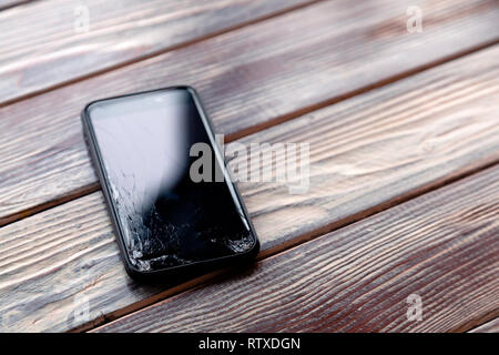 Сloseup BlackBerry-Smartphone mit ein zerbrochenes Display Glas liegen auf Holztisch. Konzept der Drop phone, gebrochen, Gadget, Elektronik Reparatur, Pech, cre Stockfoto