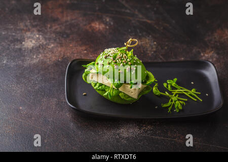 Vegan avocado Tofu Burger auf schwarzem Teller, dunklen Hintergrund. Detox gesund essen, pflanzliche Nahrung Konzept. Stockfoto