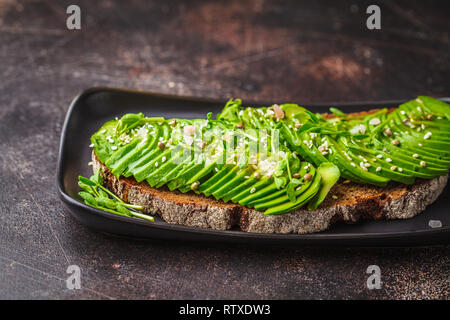 Avocado Toast mit Roggenbrot und Samen auf einer schwarzen Platte, dunklen Hintergrund. Stockfoto