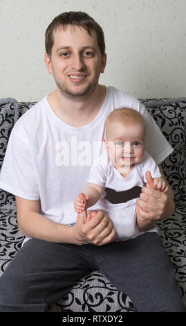 Baby sitzt auf Papa's Hände und macht lustige Gesichter Stockfoto