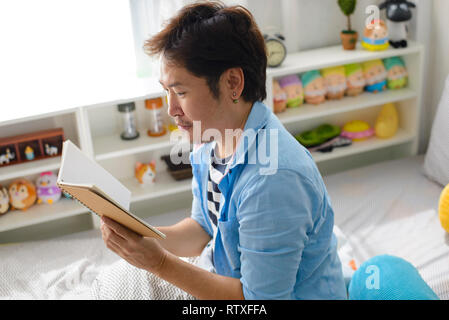 Asiatischer Mann ein Buch lesen im Bett Stockfoto