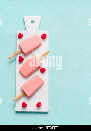 Himbeeren Joghurt Popsicle Eis auf Hellblau Türkis Hintergrund, Ansicht von oben, flach. Obst Eis. Im Sommer essen. Stockfoto