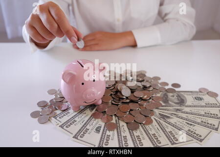 Menschen einfügen Münze in Sparschwein mit Münzen und Geld über den Schreibtisch Stockfoto