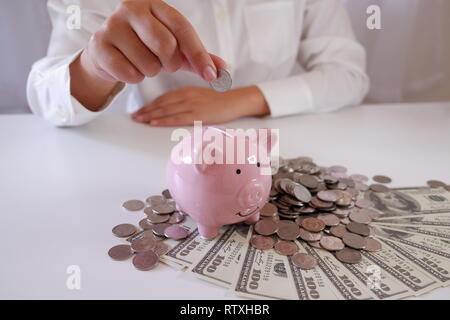 Menschen einfügen Münze in Sparschwein mit Münzen und Geld über den Schreibtisch Stockfoto