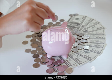 Menschen einfügen Münze in Sparschwein mit Münzen und Geld über den Schreibtisch Stockfoto