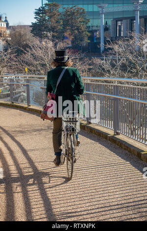 Exzentrisch Mann mit einem Hut und das Tragen eines Green Velvet Jacket reiten Pushbike an Kohle Tropfen Yard, Kings Cross, London, England gekleidet. Stockfoto