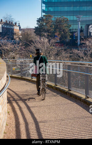 Exzentrisch Mann mit einem Hut und das Tragen eines Green Velvet Jacket reiten Pushbike an Kohle Tropfen Yard, Kings Cross, London, England gekleidet. Stockfoto