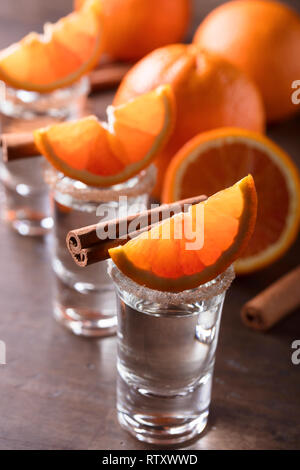 Gläser tequila mit Orangenscheiben und Zimtstangen auf einem Holztisch. Stockfoto