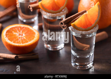 Gläser tequila mit Orangenscheiben und Zimtstangen auf einem Holztisch. Stockfoto