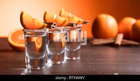 Gläser tequila mit Orangenscheiben und Zimtstangen auf einem Holztisch. Stockfoto