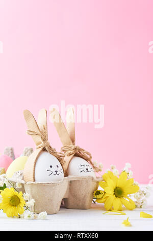 Ostern bunte Eier mit bemalten Gesichtern in Papierfach mit decorationd auf rosa Hintergrund Stockfoto