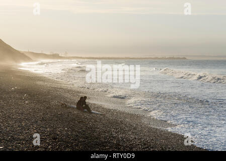 Zwei junge Surfer am Strand zu sitzen in Saltburn-by-the-Sea, North Yorkshire, England. Goldenes Sonnenlicht auf einen späten Frühling Nachmittag. Stockfoto