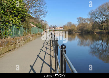 Geländer entlang des Flusses in Shrewsbury zeigt starke Schatten auf dem Weg und einem klaren blauen Himmel Stockfoto