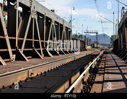 Blick von der alten Eisenbahnbrücke, Braun von Rost, Schienen, Kabel und elektrische Beiträge in Ferne sichtbar. Stockfoto