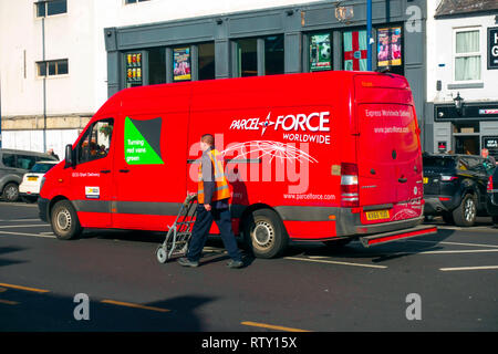 Postman Drücken einer Sackkarre in die Mail von seinem geparkten Parcelforce rot van Stockfoto