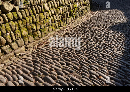 Devon, England, UK. Februar 2019. Straße mit Kopfsteinpflaster im Sonnenlicht mit einer Wand aus Granit blöcken Stockfoto