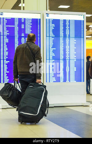 Passagiere mit Gepäck unter Fahrplan Ankunft oder Abreise in Flughafen suchen Stockfoto