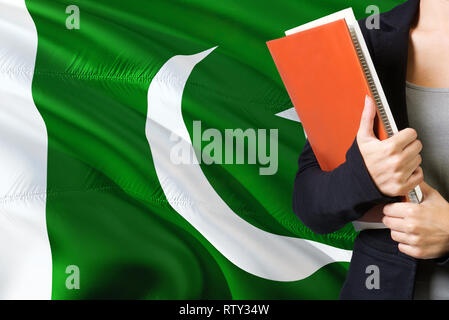 Lernen pakistanischen Sprache Konzept. Junge Frau, die mit dem pakistanischen Flagge im Hintergrund. Lehrer, orange leer Buchen Sie abdecken. Stockfoto