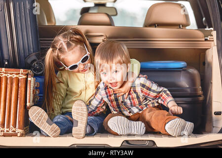 Zwei adorable kaukasischen Kinder im Kofferraum eines Autos sitzen, bevor Sie in den Urlaub mit ihren Eltern. Zwei Kinder freuen uns für eine Fahrt oder Reise. S Stockfoto