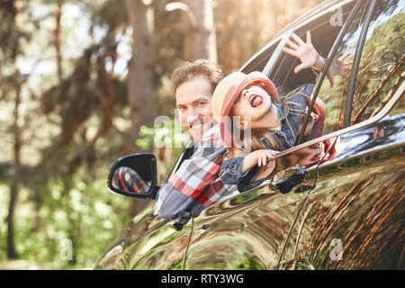 Süße kleine kaukasische Mädchen mit Hut und ihr Vater, der in kariertem Hemd schauen aus dem Fenster, während im Inneren des schwarz glänzenden Auto sitzen. Mann drivin Stockfoto