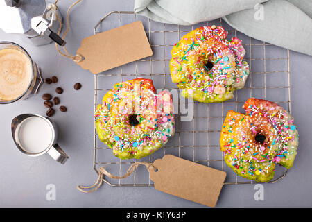 Bunt und festlich Einhorn Donut mit Streuseln auf ein Backblech Rack mit Kaffee und Bäckerei tags, Einhorn essen Trend Stockfoto