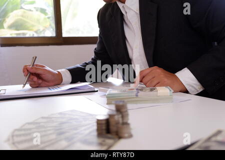 Geschäftsmann mit Taschenrechner mit Geld und Stapel von Münzen auf dem Schreibtisch Stockfoto