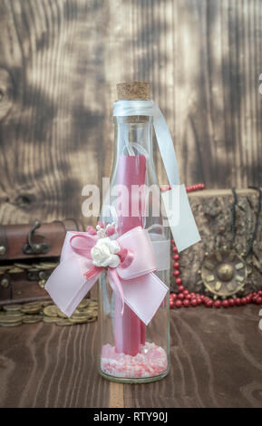 Flasche mit fettigen und Blume mit Botschaft, die hinter einer Truhe mit Schatz Perlen und Medaillon eingerichtet Stockfoto