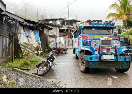 , Banaue Ifugao Provinz, Philippinen - Dezember 19, 2017: Szene bunte Jeepney fahren auf einer Straße in Banaue, umgeben von typischen armen Unterstände Stockfoto