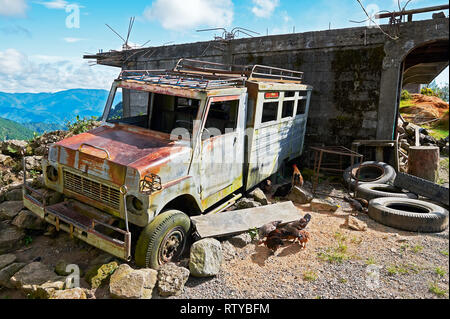 Sagada, Mountain Province, Philippinen - Dezember 5, 2010: alten, verlassenen Rusty jeepney neben einem typischen konkreten Haus auf einem Berg Stockfoto