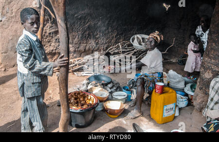 Ein schönes Foto von einer ghanaischen Familie in ihrer Küche zu Hause. Ein Junge in den Vordergrund trägt ein schmutzig. Mutter ist die Vorbereitung einer Mahlzeit auf Feuer. Stockfoto