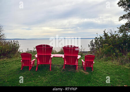 Vier rote Holzstühle sitzen zusammen an einem Aussichtspunkt mit Blick über das Wasser der Bay of Fundy im Fundy National Park New Brunswick Canada. Stockfoto