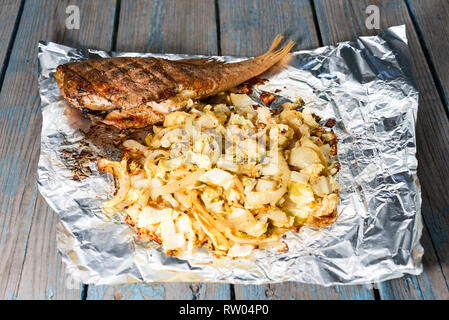 Fisch gebacken mit Gemüse liegt in eine Folie auf einem Holztisch Stockfoto