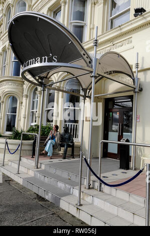 Ein Besucher sitzt neben lebensechten Statue am hotelÕs Eingang sitzen ist eine der Insel der berühmte Bewohner des Menschen, TV und Film Komödie Schauspieler, Sir Stockfoto