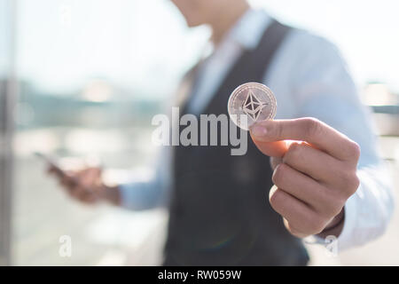 Des Astraleums cryptocurrency Münze in einen jungen Geschäftsmann Hand. Disruptive Technologie blockchain Konzept und Transfer von Reichtum. Stockfoto