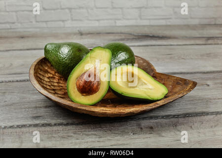 Avocado halbieren, Samen und Zellstoff sichtbar, zwei weitere ganze Birnen aus Holz geschnitzte Schüssel. Stockfoto