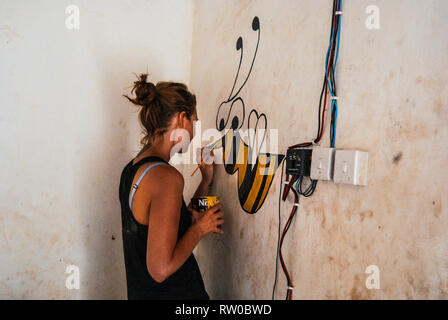 Ein kaukasischer Frau Malerei eine schöne Hummel auf einer Wand eines lokalen Volksschule Dorf im Kongo, Ghana. Stockfoto