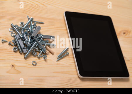 Folie von Schrauben und Muttern und einen Tablet-PC mit einem leeren Bildschirm liegen auf dem Tisch Stockfoto