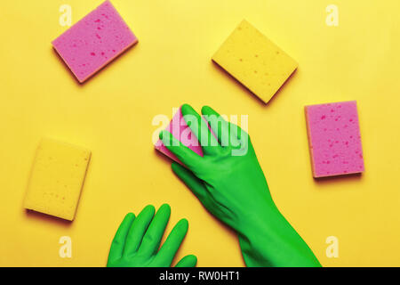 Hand in schützenden grünen Handschuh mit rosa und gelbe Schwämme auf gelbem Hintergrund Stockfoto