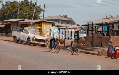 Ein Mann mit dem Fahrrad zu Fuß seinen Mantel auf einer Straße im ghanaischen Stadt Bolgatanga, West Afrika Stockfoto