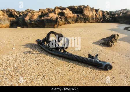 Schwarz Schnorcheln und Tauchen am Strand sand, kleinen Felsen im Hintergrund. Durch nasses objektiv Geschossen (Tropfen, Teile des Bildes unscharf) Wasser zu betonen. Stockfoto