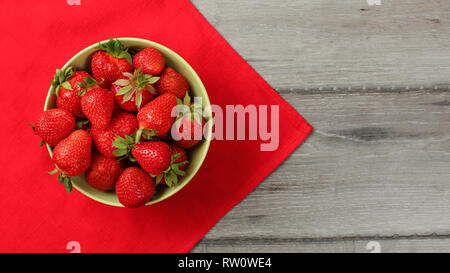 Rote reife Erdbeeren in eine kleine Schüssel geben, mit Tischdecke und grauen Schreibtisch unter. Stockfoto