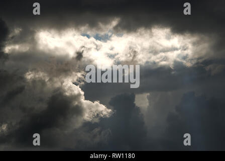 Dramatische Wolkenbildung, bei der die Sonne durch einen kleinen Wolkenbruch scheint, was ein spektakuläres Bild von Lichtform und Farbe gibt Stockfoto