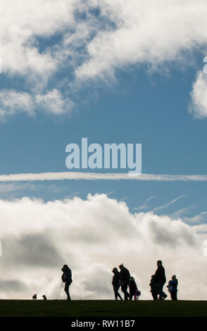 Eine Gruppe von Menschen mit zwei Hunden, die beim gehen in die Silhouette gegen eine große Wolkenbank und einen tiefen blauen Himmel geraten sind Stockfoto