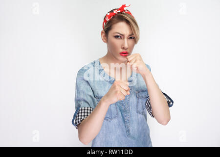 Porträt von Ernst schöne junge Frau in lässigem Blue Denim Shirt mit Make-up und roten Stirnband mit Boxing Faust und Kamera. ind Stockfoto