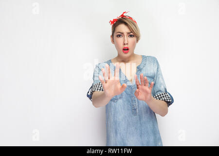 Portrait von schockiert, schöne junge Frau in lässigem Blue Denim Shirt mit Make-up und roten Stirnband stehend, Angst, hob die Arme und Kamera. Stockfoto