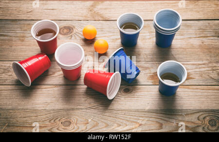 Bier pong, college Party Game. Kunststoff rot und blau Tassen und Ping Pong Bälle auf Holz- Hintergrund Stockfoto