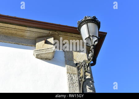 Schwarzes Eisen Licht und Sonnenuhr auf einer Mauer aus Stein mit blauen Himmel. Ponte Maceira, Provinz La Coruna, Spanien. Stockfoto
