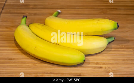 Drei Bananen auf einem woden Schneidbrett auf Granit Zähler Stockfoto